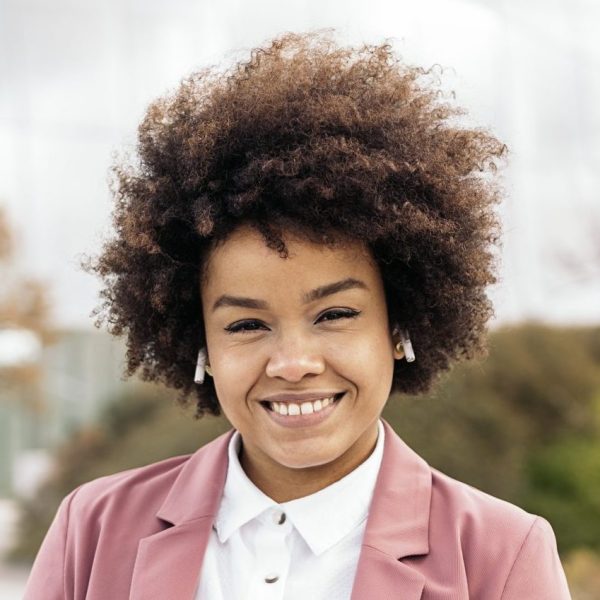 Pretty black business woman with afro hair holding her laptop and looking at camera. She is walking in a business area of the city.